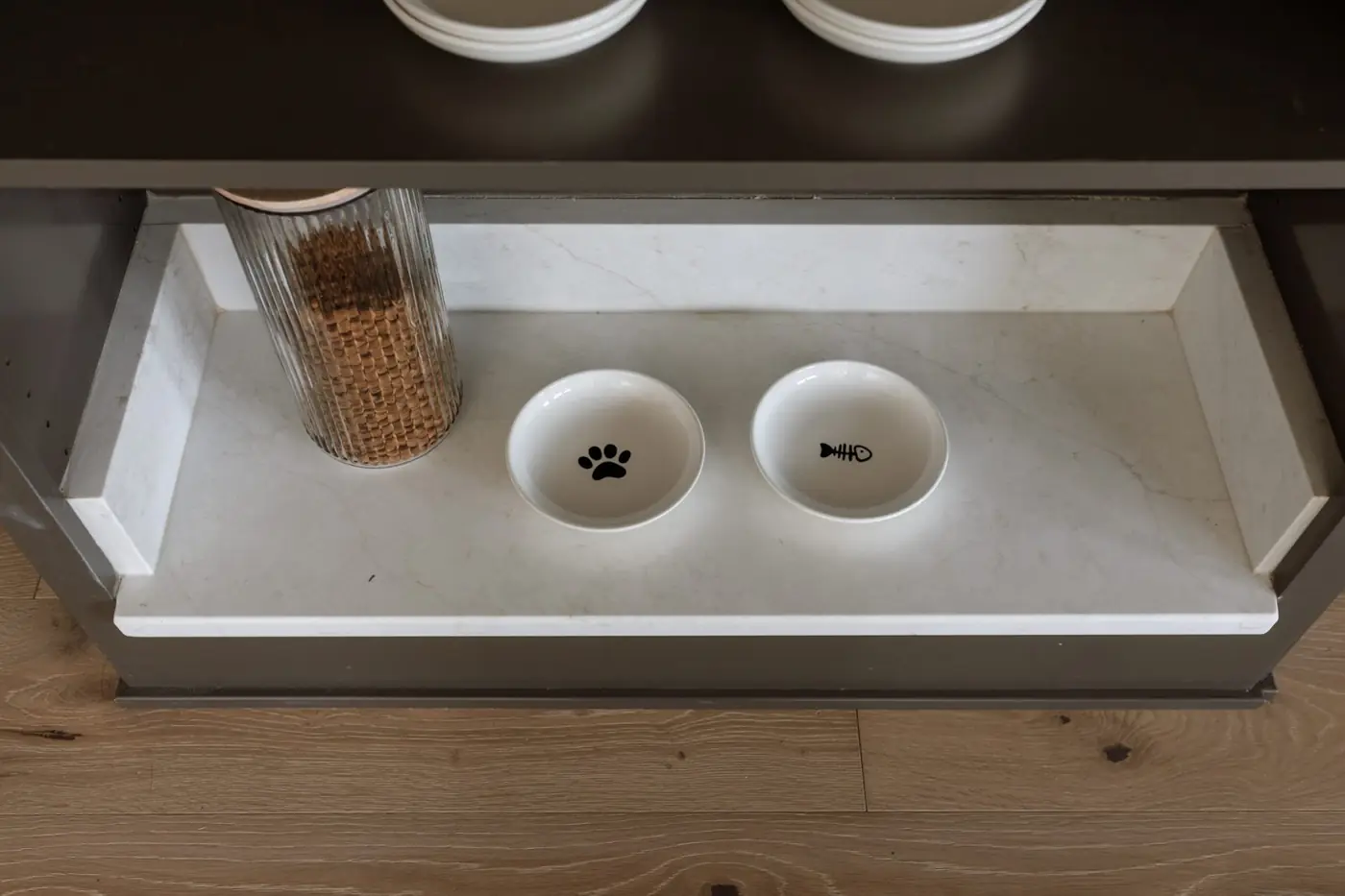 Built-in quartz cat feeding station with paw and fish bowls tucked into the kitchen island