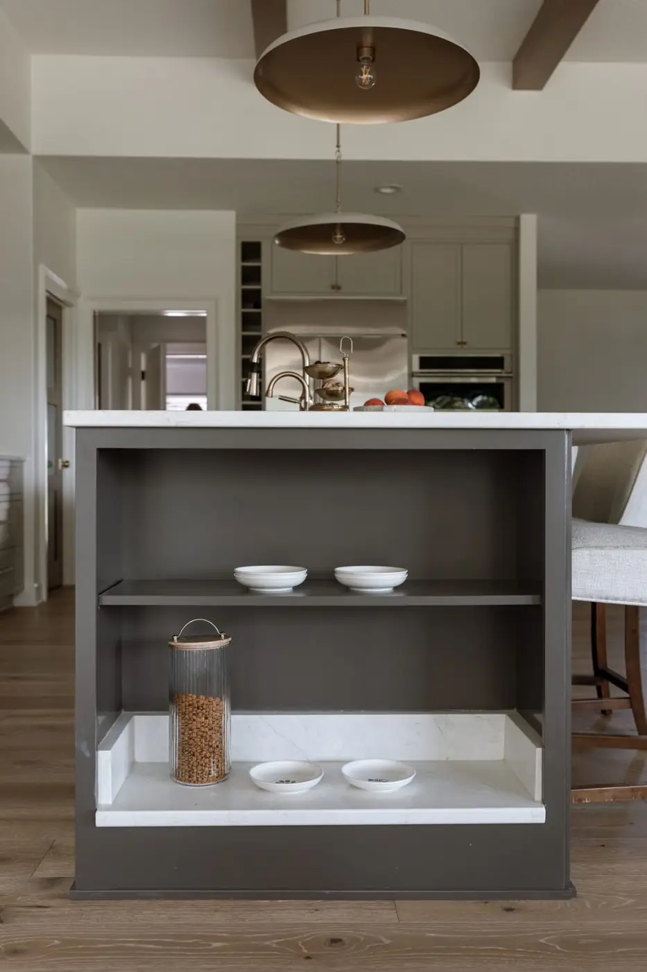 End of the kitchen island with open shelving and a quartz-lined cat feeding station at floor level