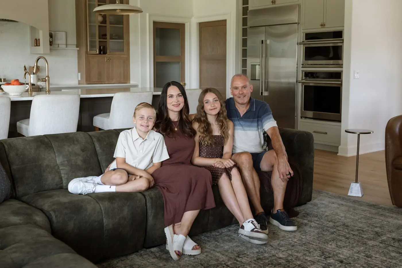 The Ludwig family on a green velvet sectional in the great room with the kitchen behind them