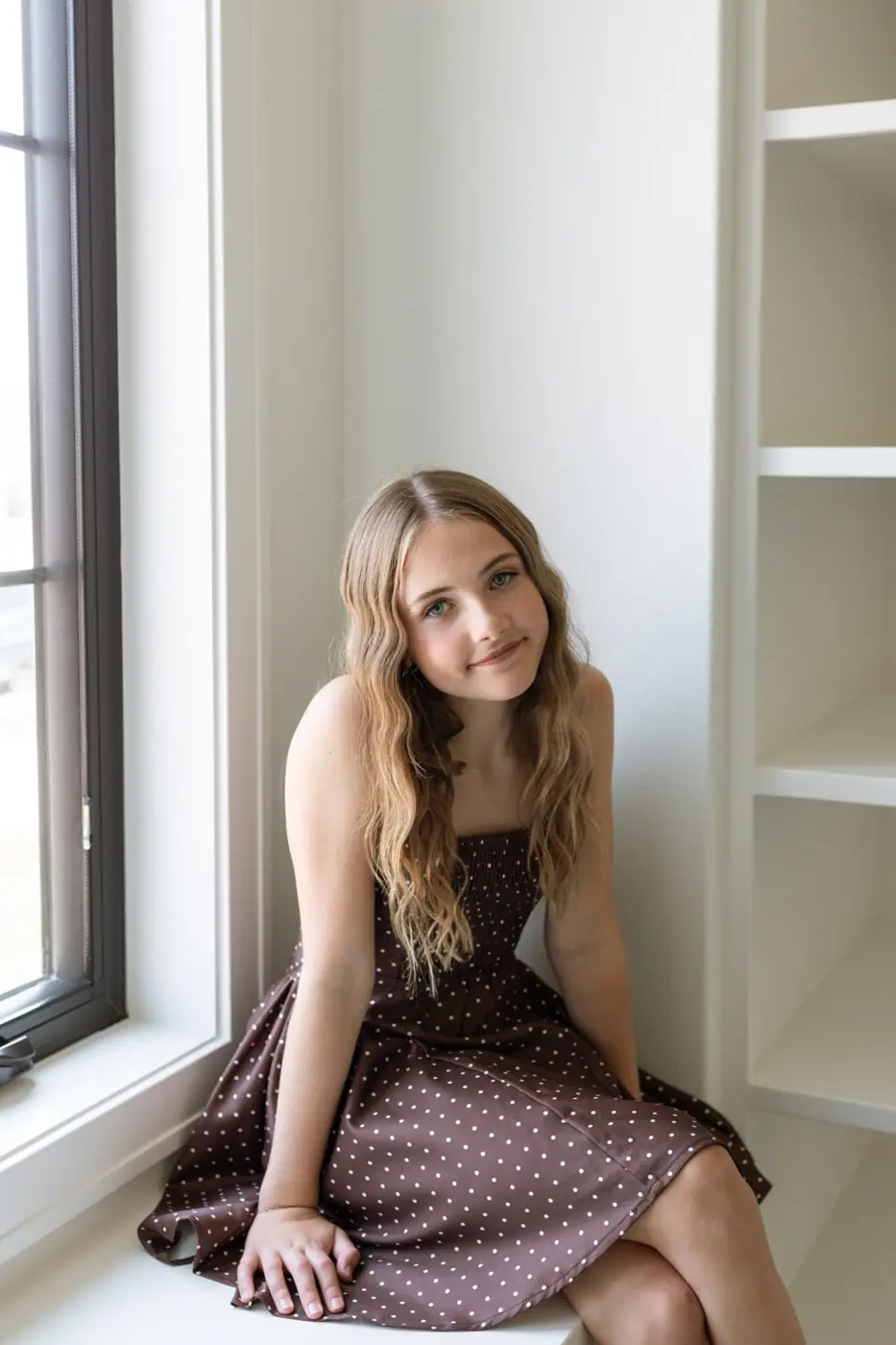 Jules Ludwig sitting in the built-in window seat in her bedroom with display shelves