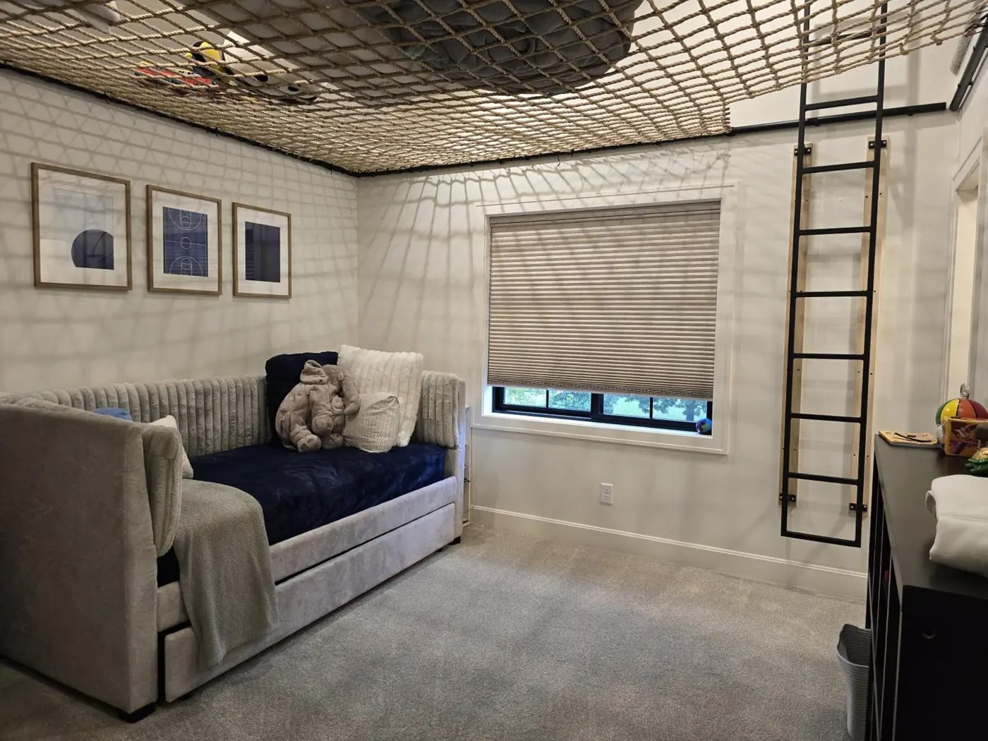 Boy's bedroom with a rope climbing net stretched across the vaulted ceiling, a black wall ladder, navy daybed and basketball art