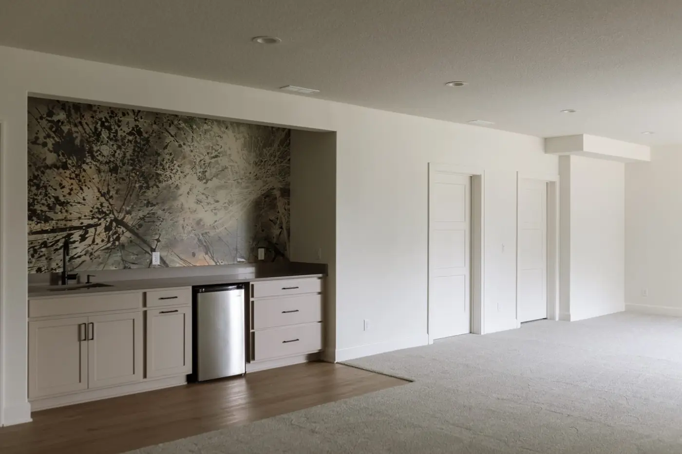 Finished lower level with a snack wet bar under botanical mural wallpaper and open play space